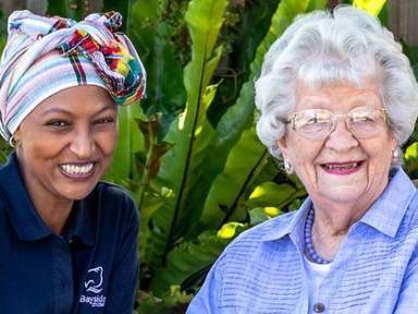 Image of an aged care worker and an elderly resident sitting together smiling at the camera