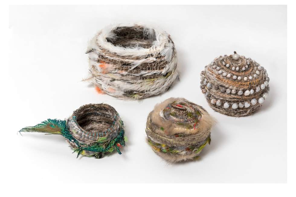 Four baskets of various sizes woven with feathers, seeds and grass.