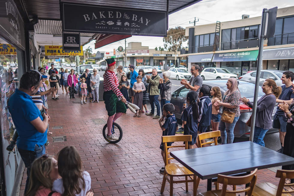 Performer with juggling sticks on a unicycle entertaining children in Black Rock village.