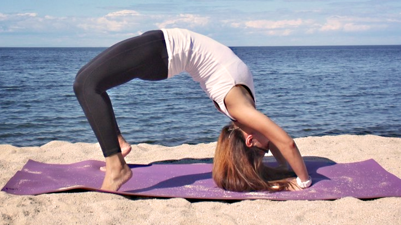Young person on beach doing a backbend yoga move on a purple yoga mat