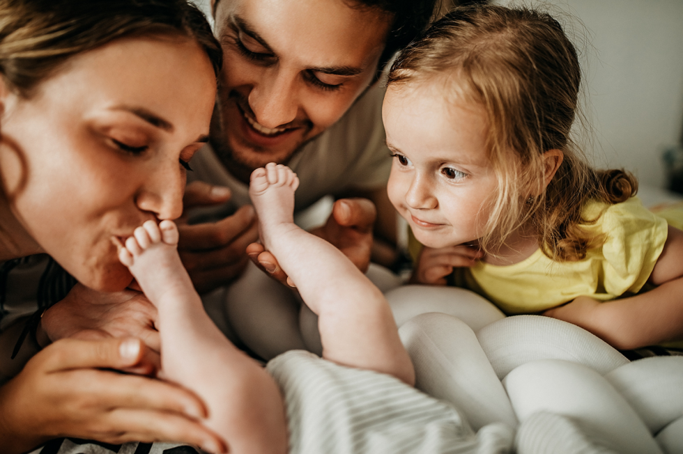 Parents kissing baby's feet with toddler looking on