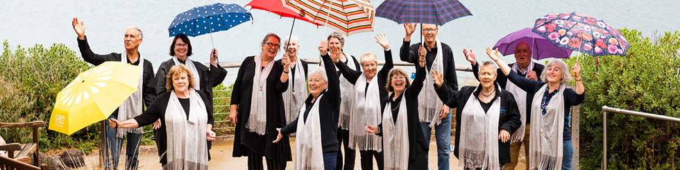 a group of mature aged performers dressed in black and white holding colourful umbrellas 