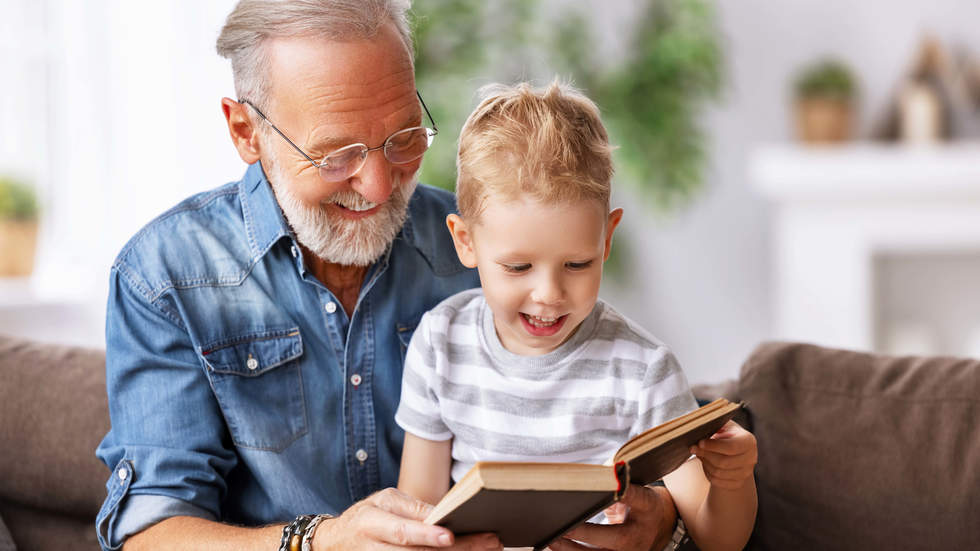 Grandpa reading book to grandson. Both are smiling.