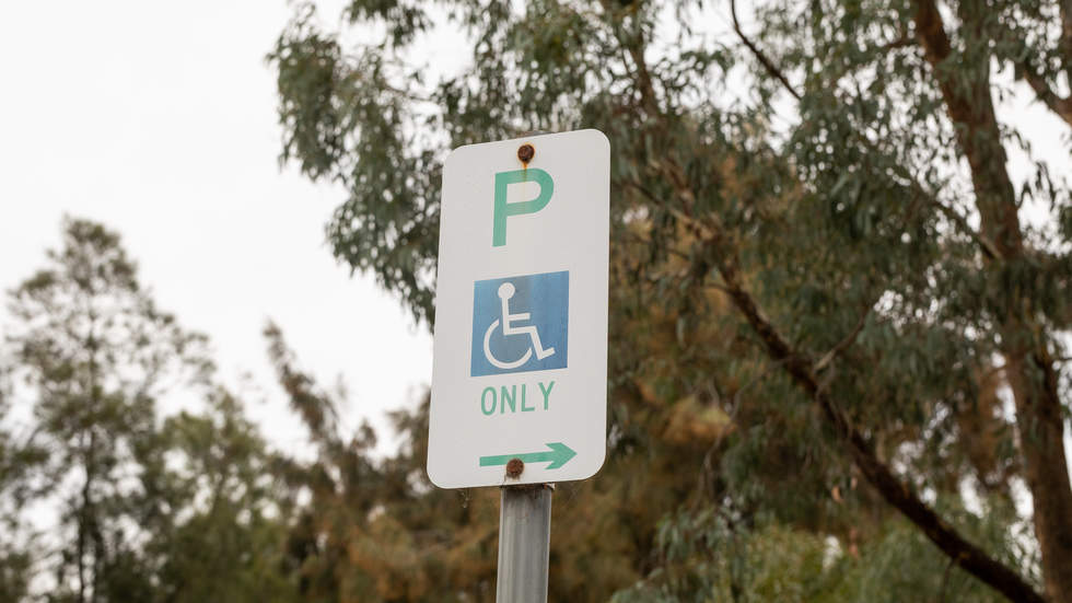 Accessible parking space sign with tree canopy in background