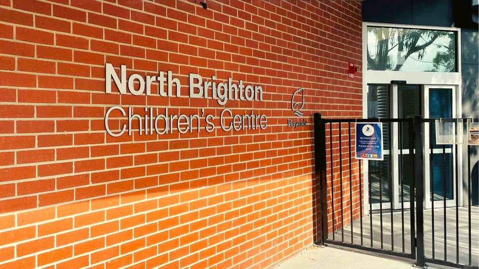 North Brighton Childrens Centre entrance, name and Bayside Council logo displayed on a red brick wall to the left and black security fence on the right