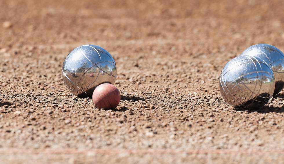 Silver petanque balls surrounding the target ball on a gravel petanque piste.