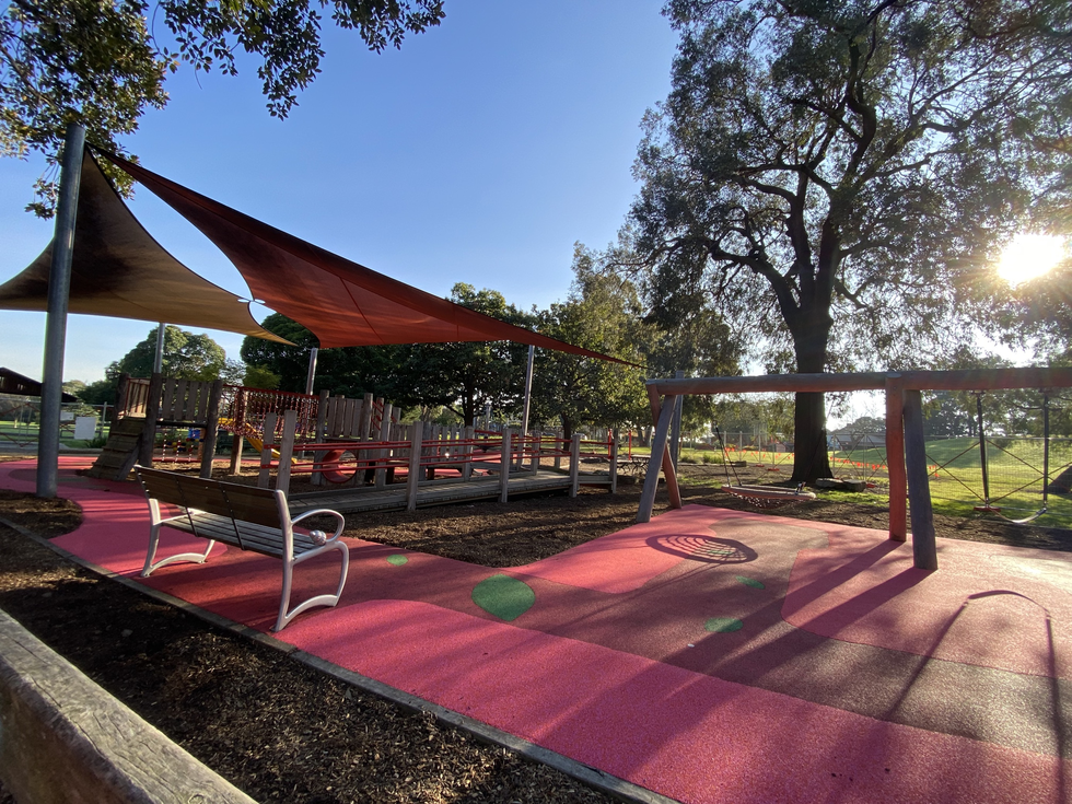 New play equipment at Landcox Park playground with swings, a multi use play area, red rubber matting and triangle shade cloths.