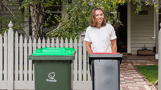 Person wheeling out their red lidded general waste bin 