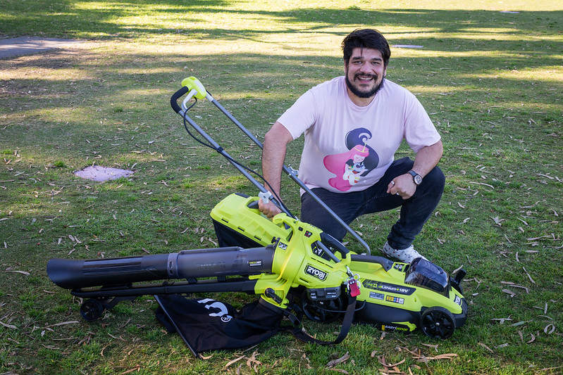 A person kneeling behind an electric lawnmower and leaf blower