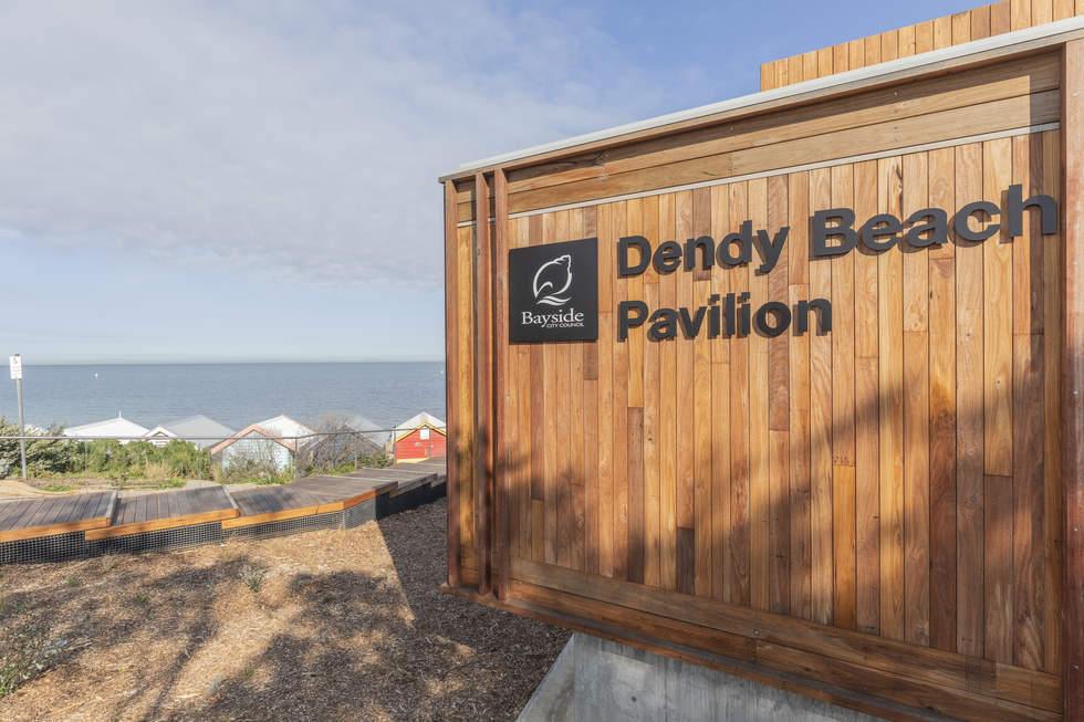 Dency Beach Pavilion external signage with Brighton Bathing Boxes and beach in the background.