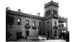 Black and white photo of an old Italianate mansion with a hospital bed in the foreground.