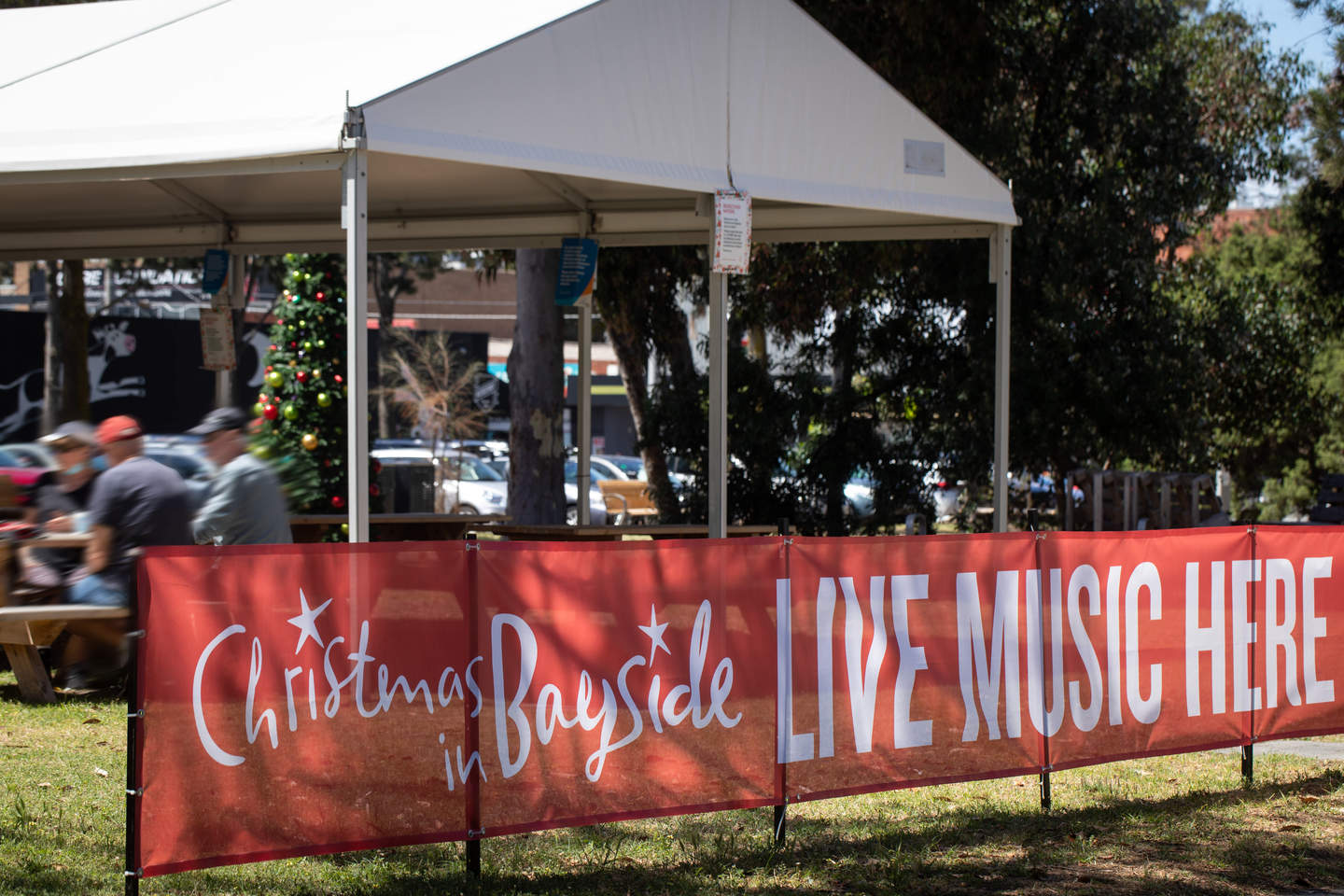 Chrismas in Bayside Live Music Here banner in front of people sat on benches.