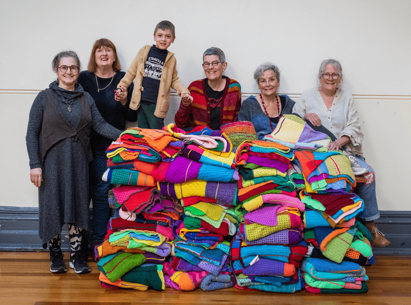 People standing behind multicoloured blankets stacked on top of each other