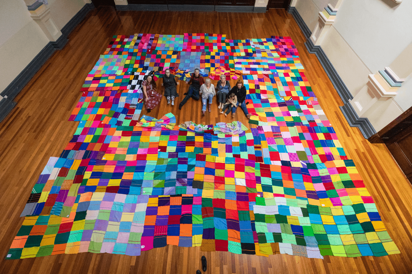 People sitting in the middle of colourful blankets spread across a wooden floor