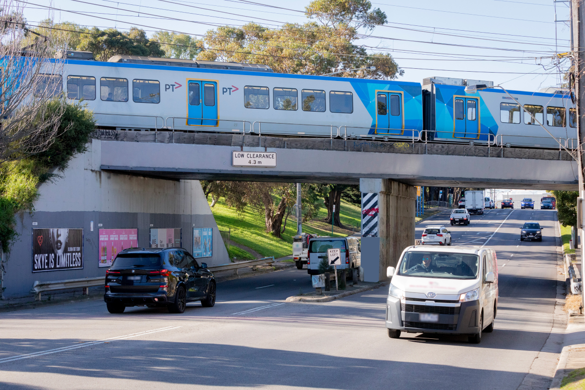 Cars driving under a bridge which has a train going over it