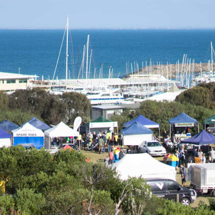 View of market stalls in the backdrop of a marina filled with yachts.