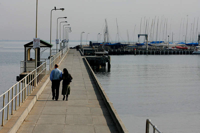 A man and woman walk along Middle Brighton Pier