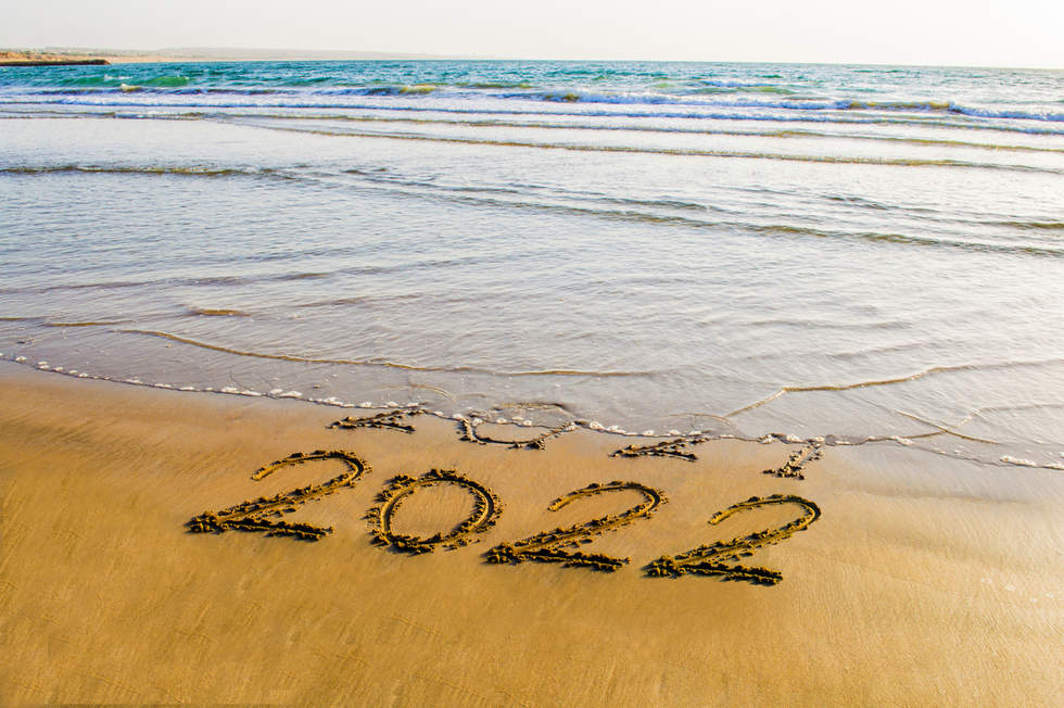 Waves washing away 2021 written on the sand. 2022, written underneath is fully visible.