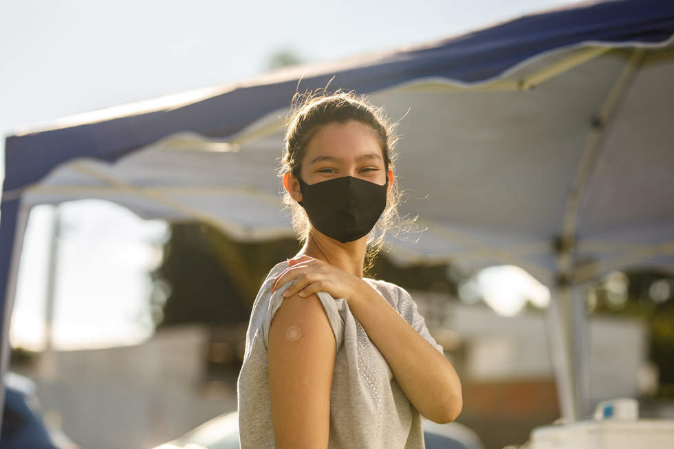 Young woman masked holds up her sleeve to show band aid on her upper arm