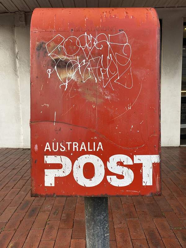 Red Australia Post box with graffiti scratched into the metal