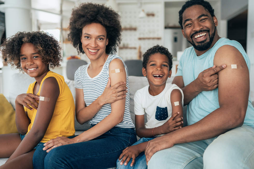 Family smiling at camera with band aids over their flu shots