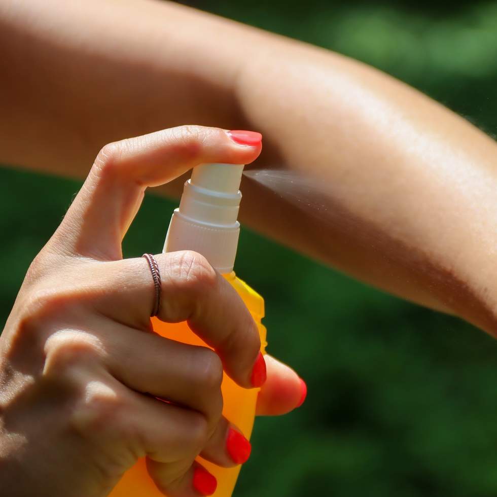Woman spraying insect repellent using yellow spray bottle
