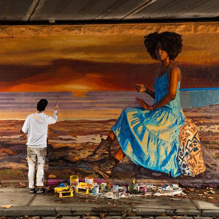 Artist painting a mural of a woman against a sunset