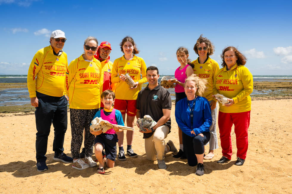 Life saving club members stand in the sand holding fossils