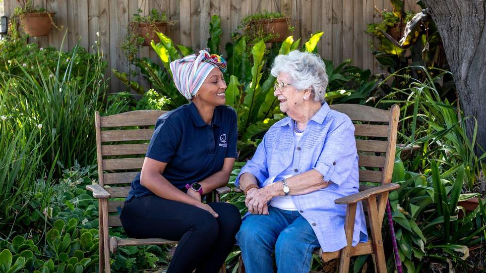 A care worker and older lady sitting the garden having a chat.