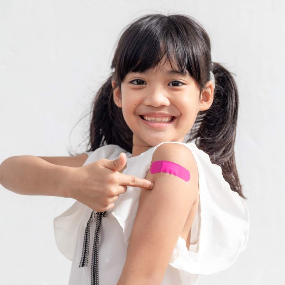 A young girl pointing to a band aid on her arm after a vaccination.